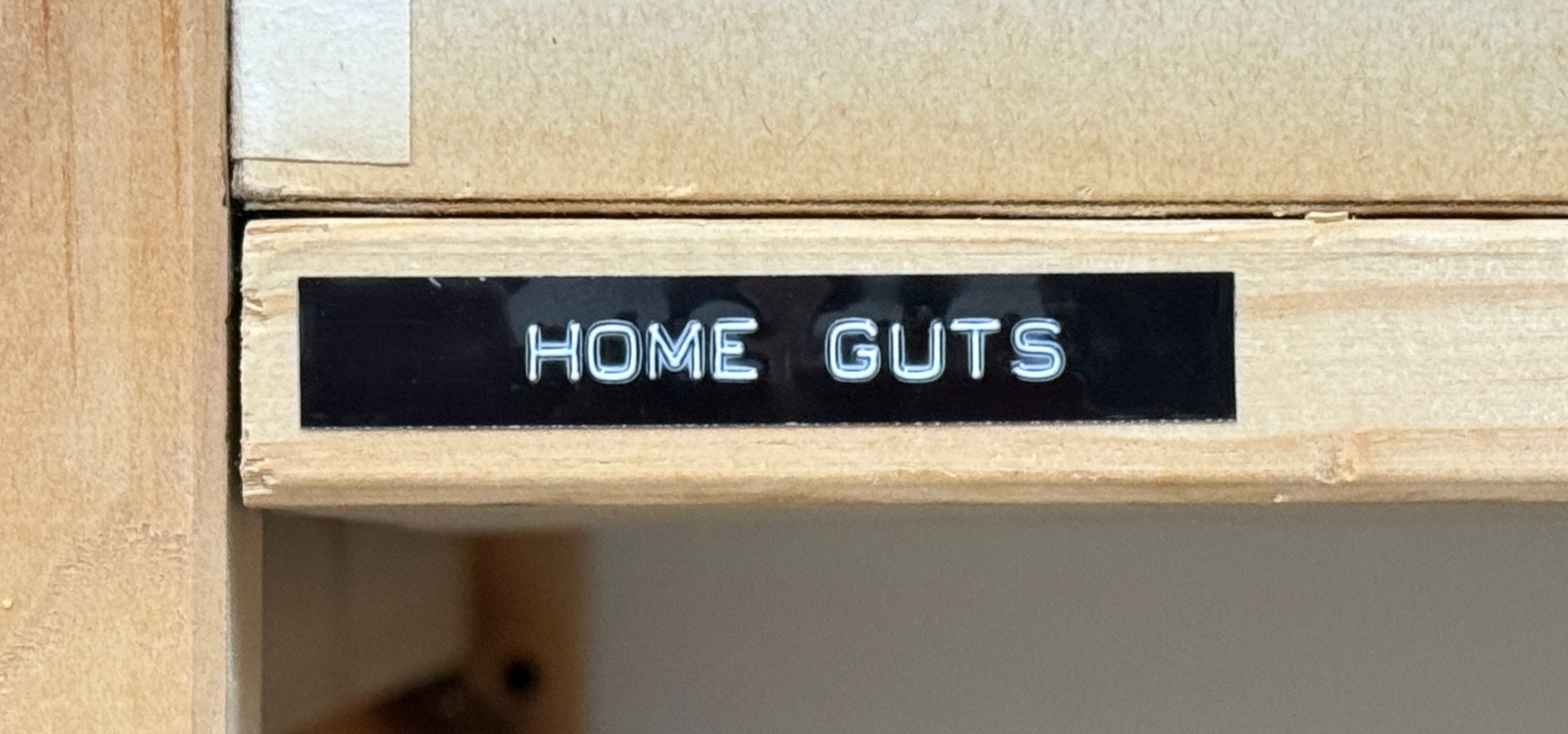 Wooden shelf with 'HOME GUTS' label on a neutral background